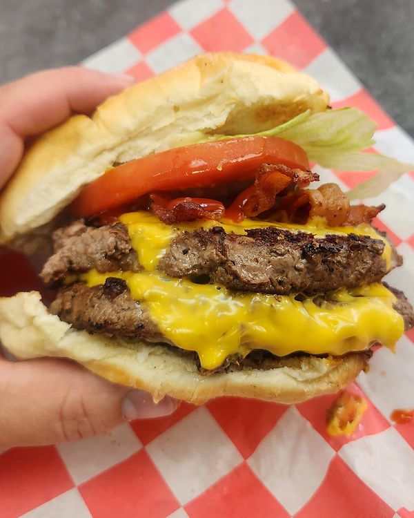 Close-up of a double cheeseburger with bacon, lettuce and tomato on red-checkered paper