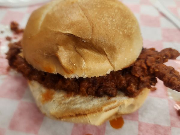 Buffalo chicken sandwich: fried chicken in buffalo hot sauce on a soft bun, on pink-checkered paper